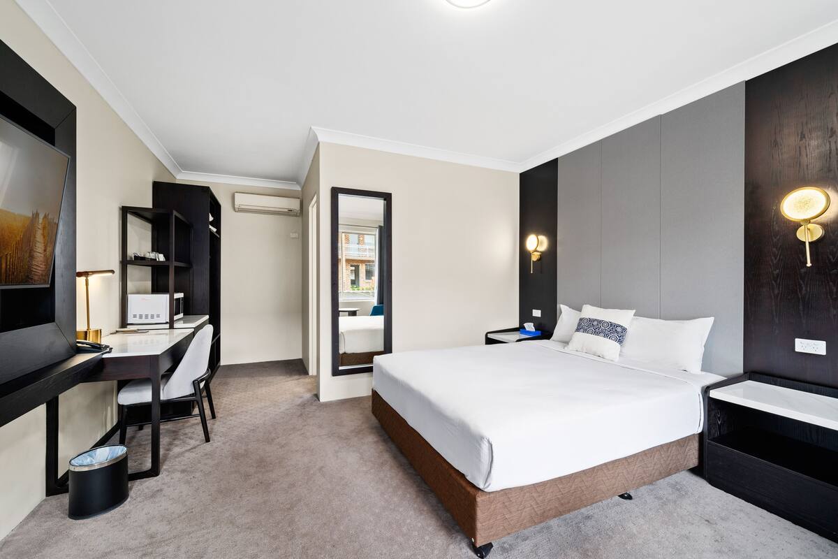 A hotel room with a bed, desk, chair, and a television.