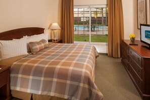 Hotelkamer met een bed, nachtkastje, kapstok, televisie en raam met uitzicht op een zwembad en terras.