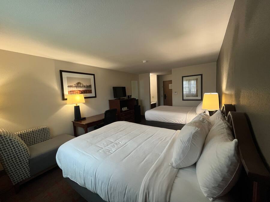 A hotel room with two beds, a desk, a chair, and a sofa.