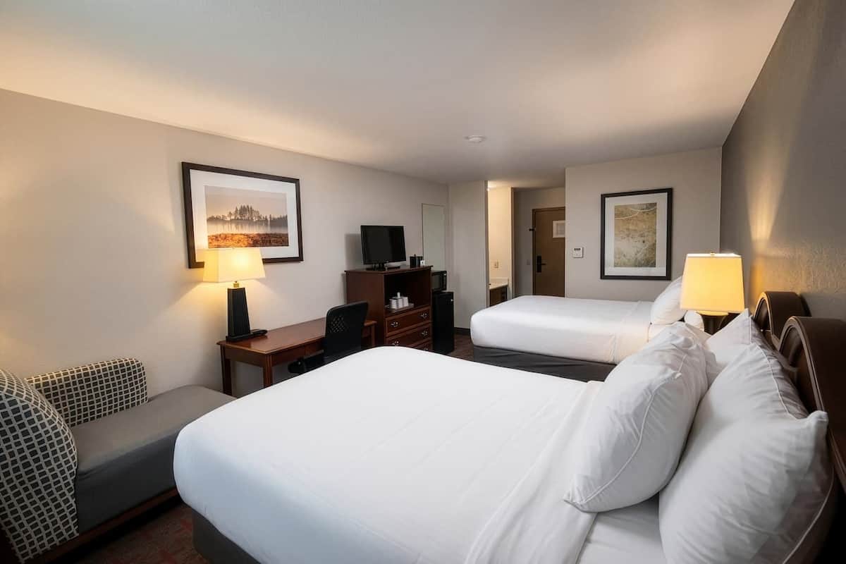 A hotel room with two beds, a desk, a chair, a TV, and framed pictures on the walls.
