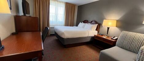 A hotel room with a bed, desk, chair, and a sofa.