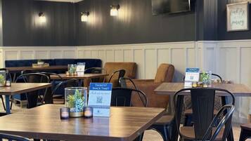 Interior de restaurante com mesas, cadeiras e um espaço reservado com bancos. Placas indicam 'Sede? Hora de petiscar?' e 'Álcool de fora não é permitido'.