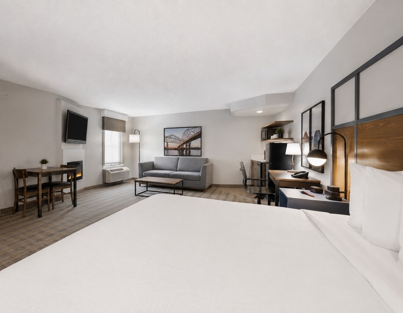 Habitación de hotel con una cama grande, un sofá, un escritorio con lámpara, un televisor y un cuadro en la pared.