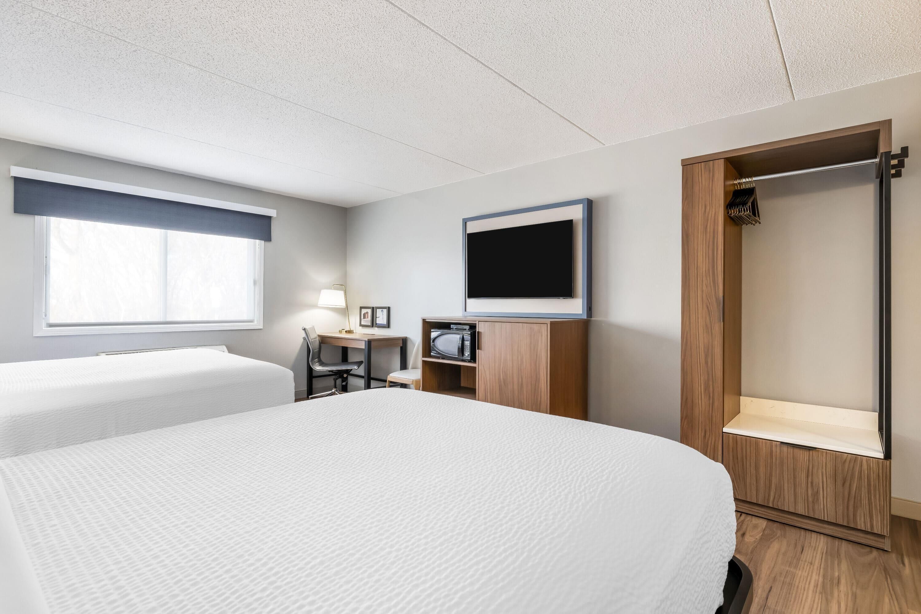 A hotel room with a large bed, a desk with a chair, a TV, a wardrobe, and a shower area.