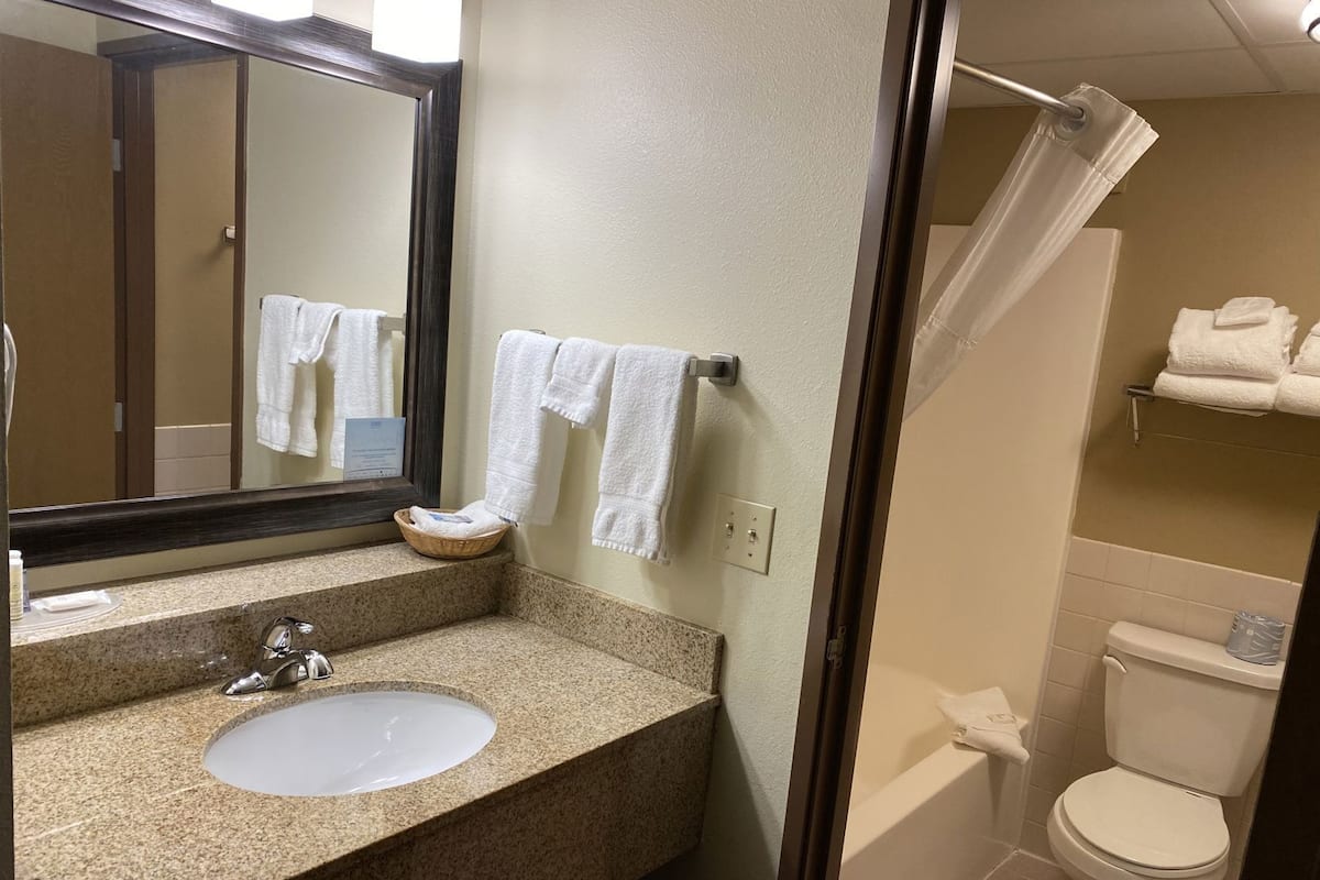 A bathroom with a granite countertop sink, a mirror, a towel rack with towels, a shower curtain, and a toilet.