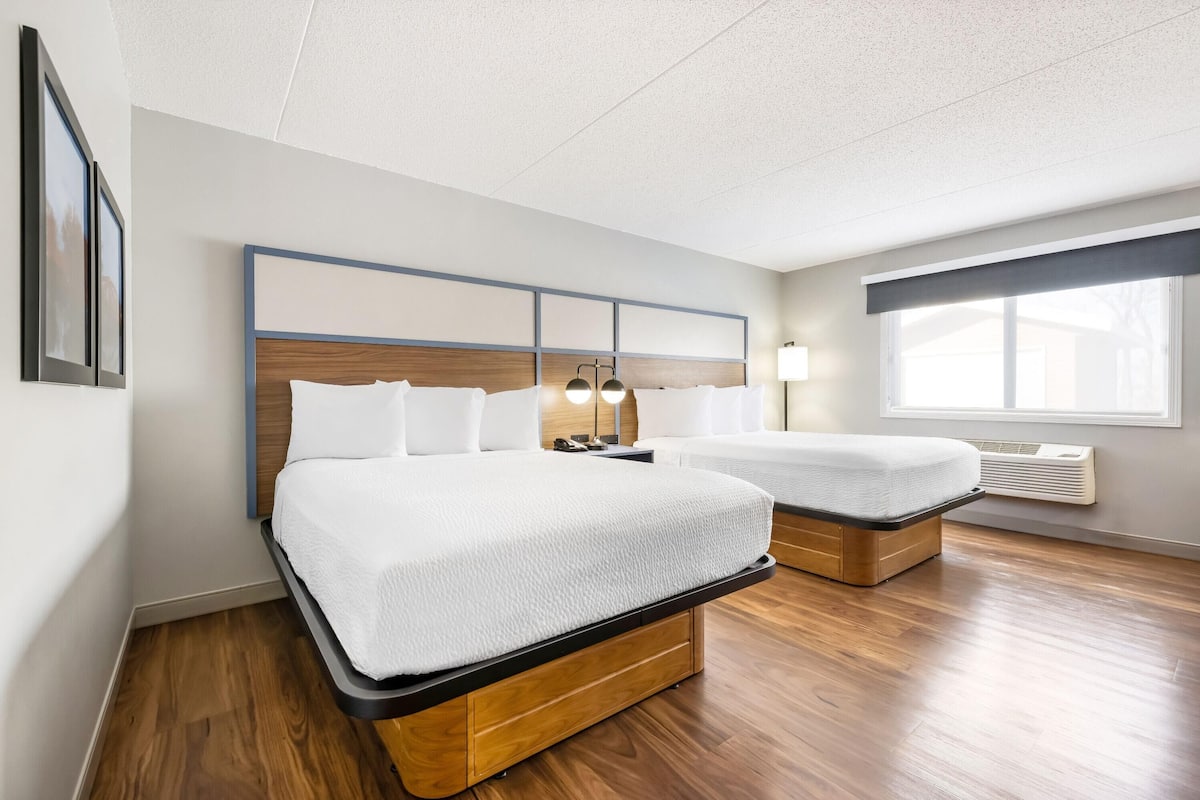 A hotel room with two beds, a wooden floor, a large window, and a ceiling with a grid pattern.