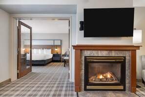 A hotel room with a fireplace, a bed, a TV, and a patterned carpet. - AmericInn by Wyndham Valley City - Conference Center (Valley City)