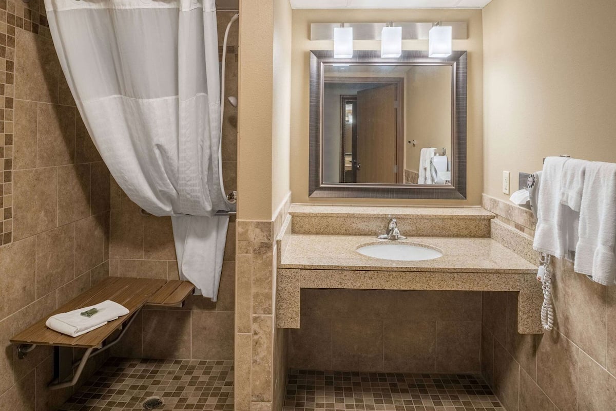 A bathroom with a shower, a sink, a mirror, and a towel rack.