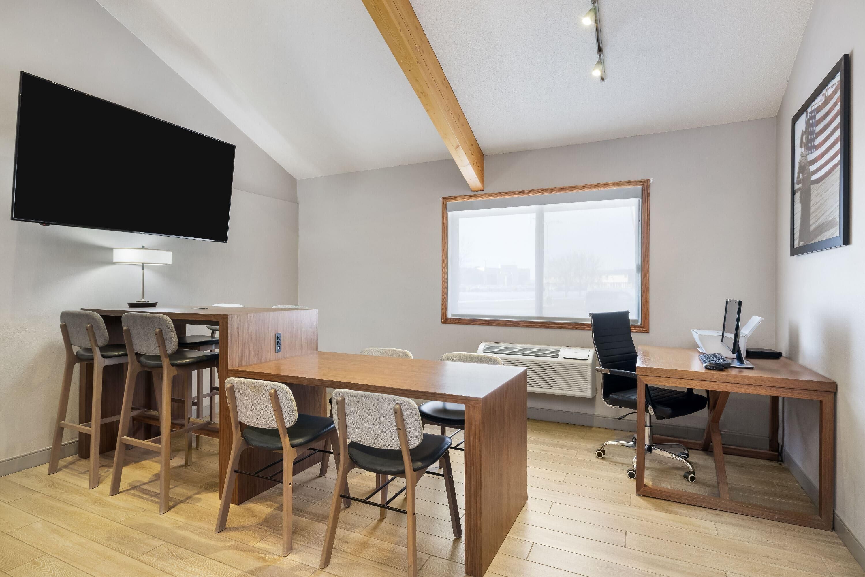 A modern office space with a large desk, chairs, a flat-screen TV, a window, and a ceiling with exposed beams.