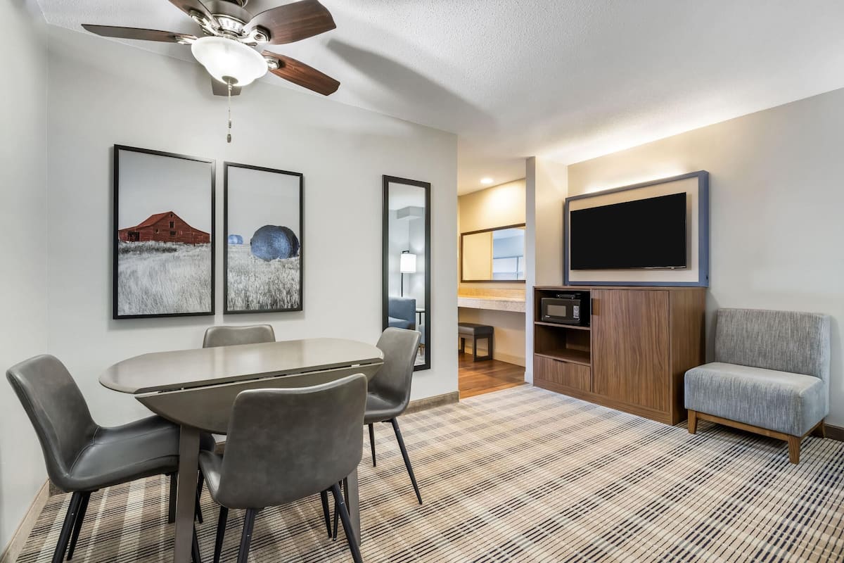 A modern living room with a dining area, a flat-screen TV mounted on the wall, and a ceiling fan.