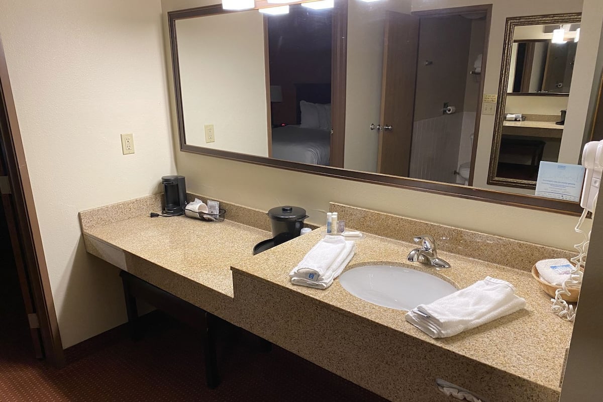 A hotel bathroom with a granite countertop sink, a large mirror, and a coffee maker.