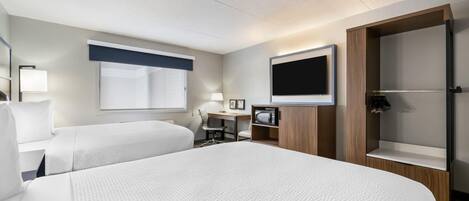 Ein Hotelzimmer mit zwei Betten, einem Schreibtisch mit Stuhl, einem Fernseher, einem Kleiderschrank und einem kleinen Tisch mit Lampe.