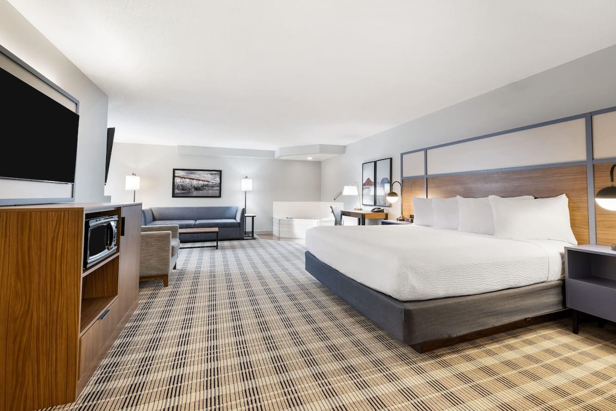 A modern hotel room with a large bed, a sofa, a desk, and a flat-screen TV.