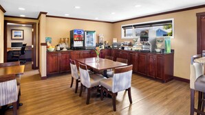 A hotel dining area with a wooden table and chairs, a coffee machine, and a refrigerator. - Quality Inn Port Angeles - near Olympic National Park (Port Angeles)