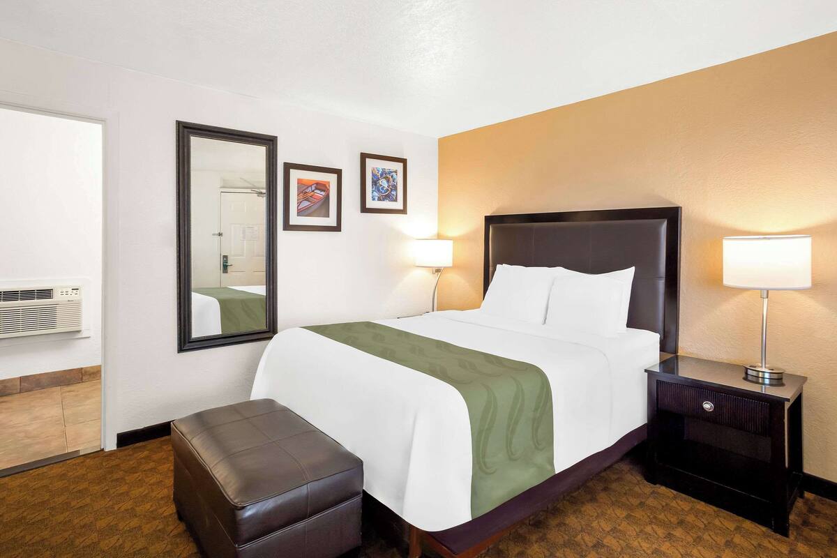 A hotel room with a large bed, two bedside lamps, a nightstand, a bench, and a mirror on the wall.