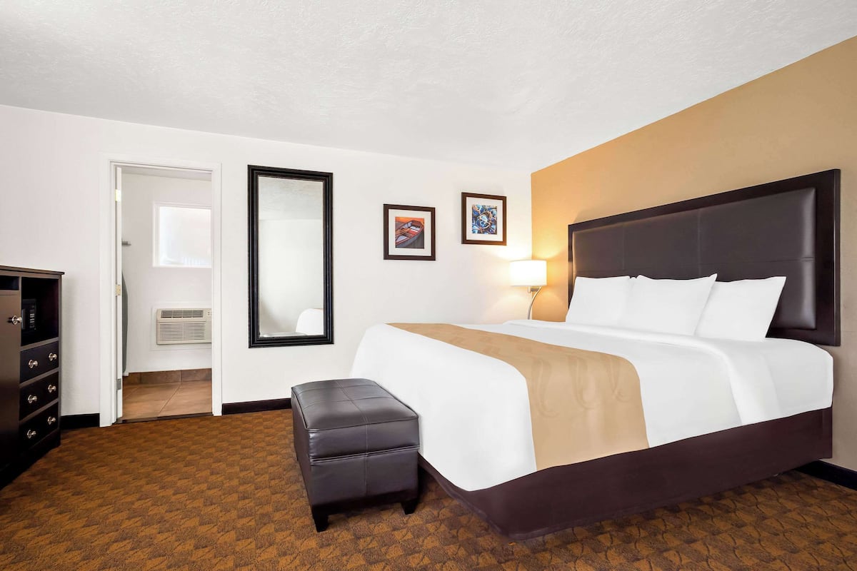 A hotel room with a large bed, a small stool, a dresser, and a door leading to a bathroom.