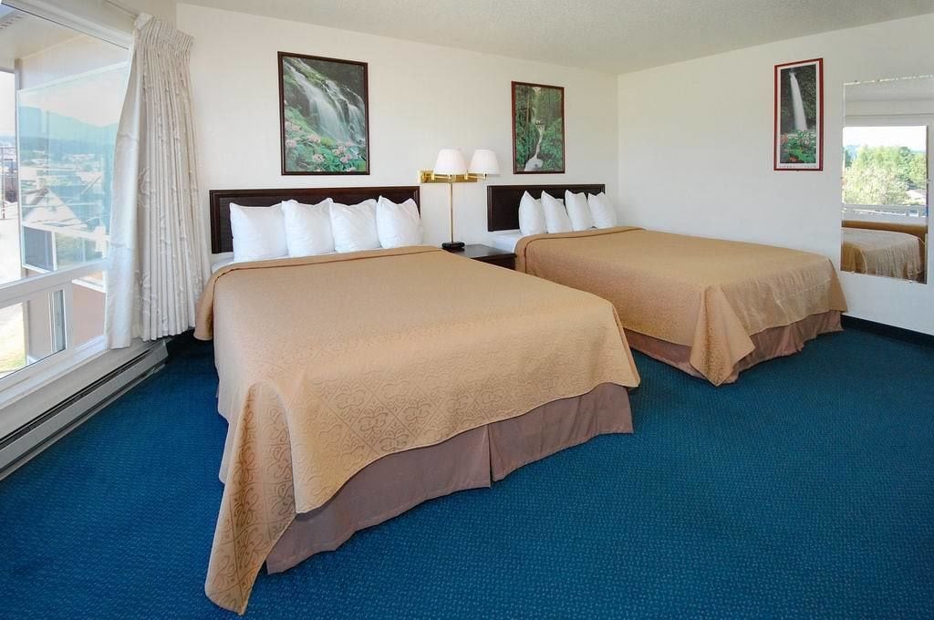 A hotel room with two beds, a large window with a view, and artwork on the walls.