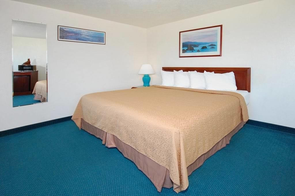 A hotel room with a large bed, a nightstand, a lamp, and two framed pictures on the wall.