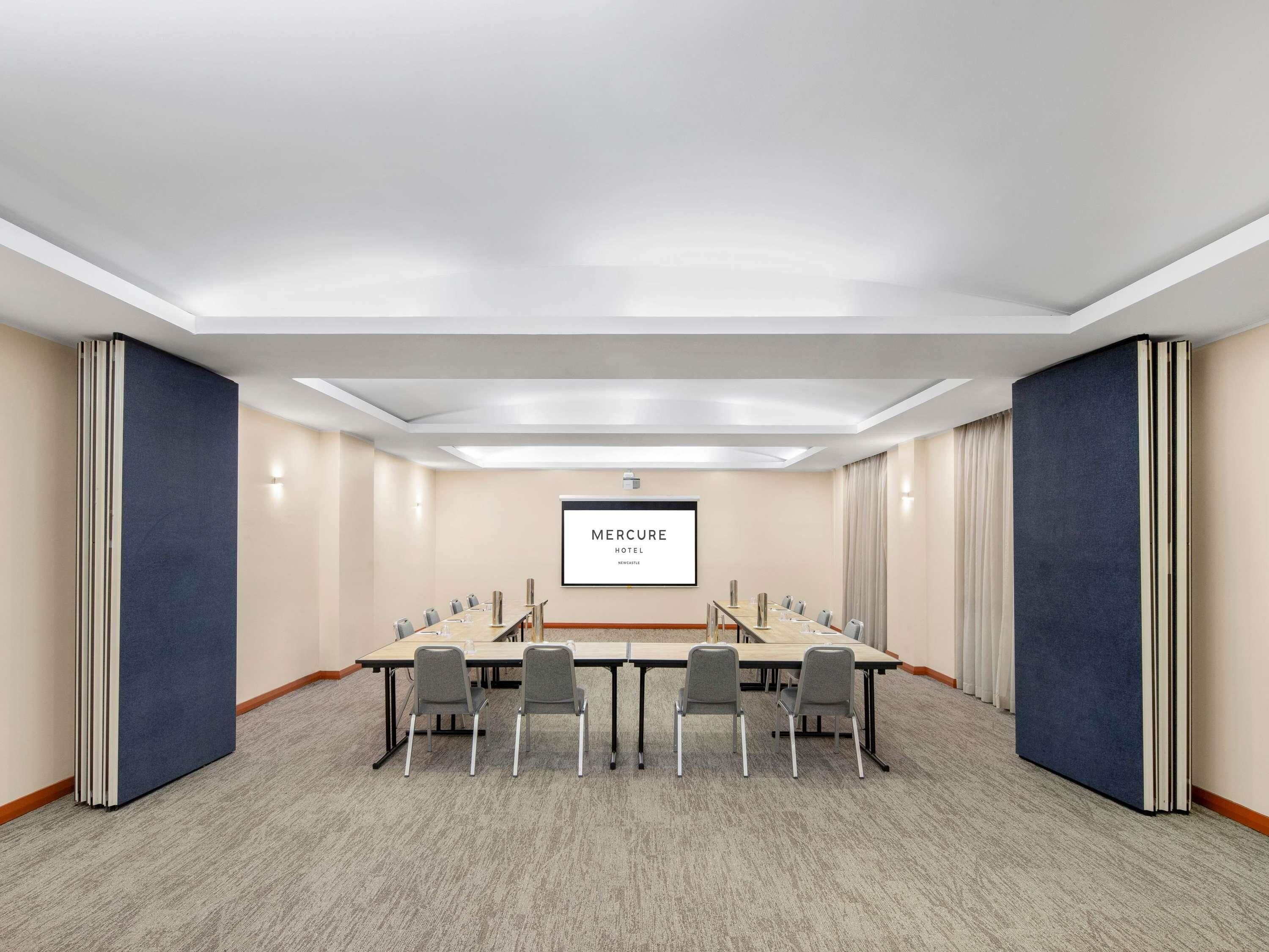 A conference room with a long table, chairs, a projector screen, and a carpeted floor.