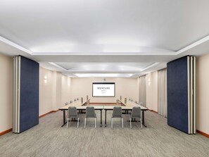 A conference room with a long table, chairs, a projector screen, and a carpeted floor. - Mercure Newcastle (Newcastle West)