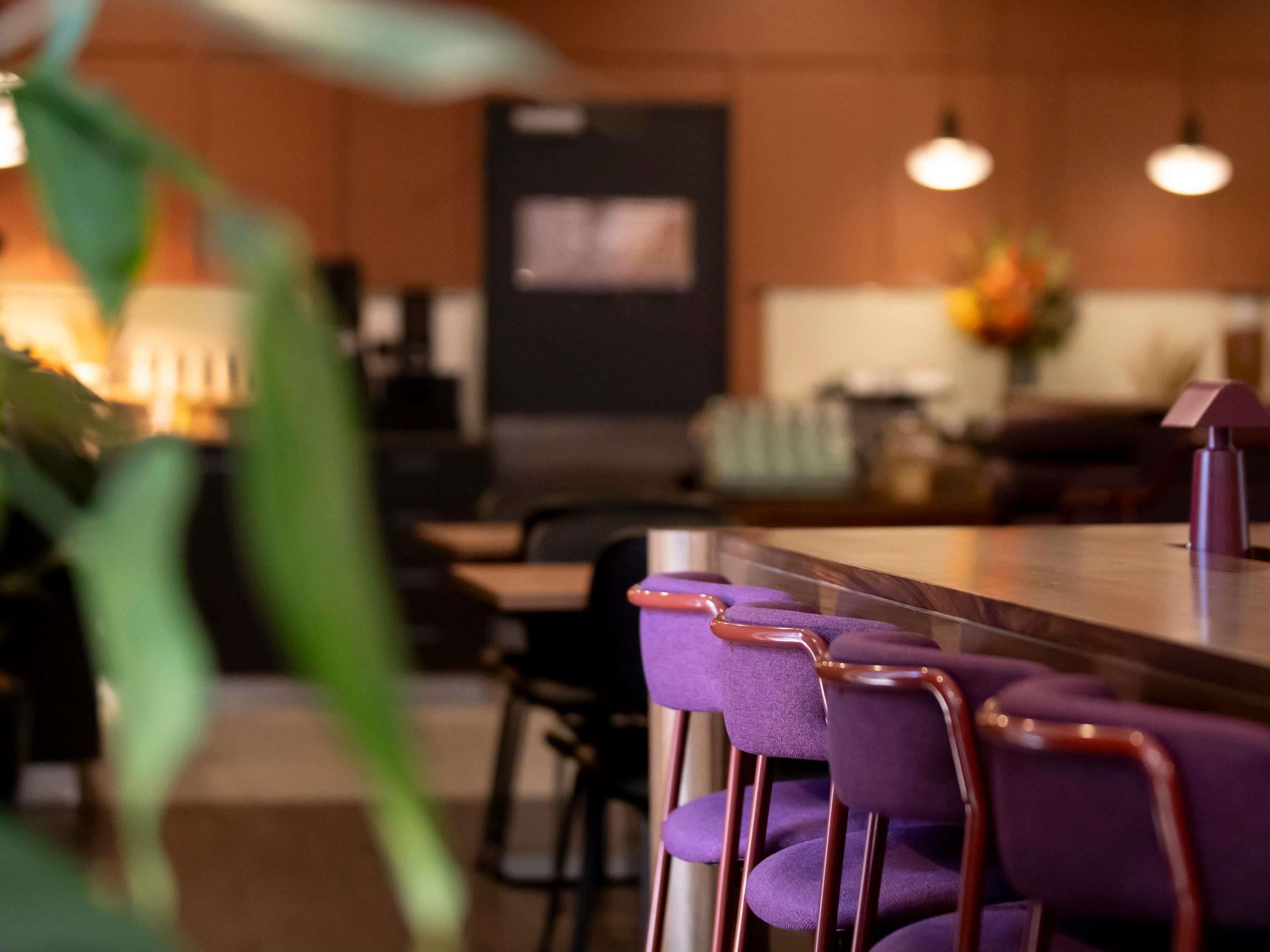 A modern kitchen with a bar area, purple bar stools, and pendant lighting.