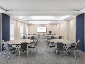 A conference room with multiple tables and chairs, a projector screen displaying 'Mercure Hotel Newcastle', and a carpeted floor. - Mercure Newcastle (Newcastle West)