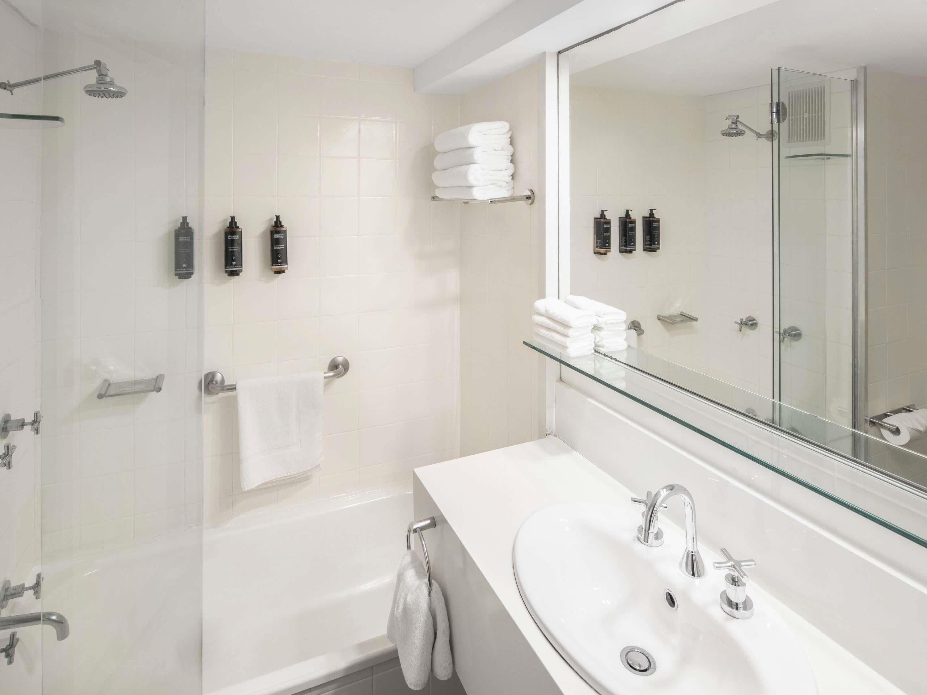 A modern bathroom with a glass shower enclosure, a bathtub, a large mirror, and a white sink.