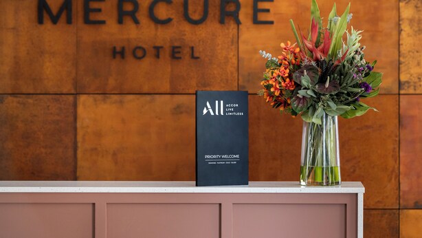 Eine Rezeption im Mercure Hotel mit einer Blumenkomposition und einem schwarzen Schild.