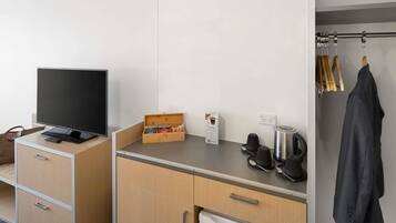 A hotel room with a flat-screen TV, a compact kitchen area with a coffee maker, a Haier refrigerator, and a coat hanging on a rack.