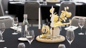 A dining table set with wine glasses, a bottle, a candle, and a centerpiece with flowers and a decorative item. - Mercure Newcastle (Newcastle West)