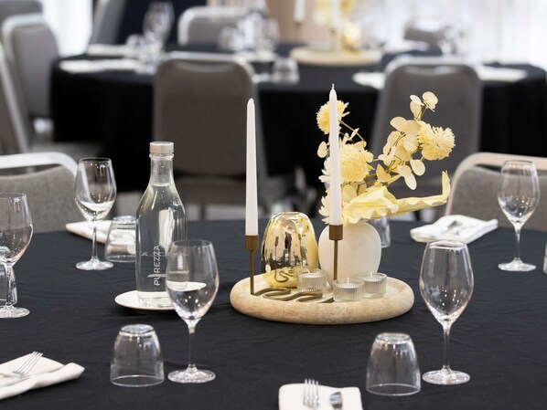 A dining table set with wine glasses, a bottle, a candle, and a centerpiece with flowers and a decorative item. - Mercure Newcastle (Newcastle West)