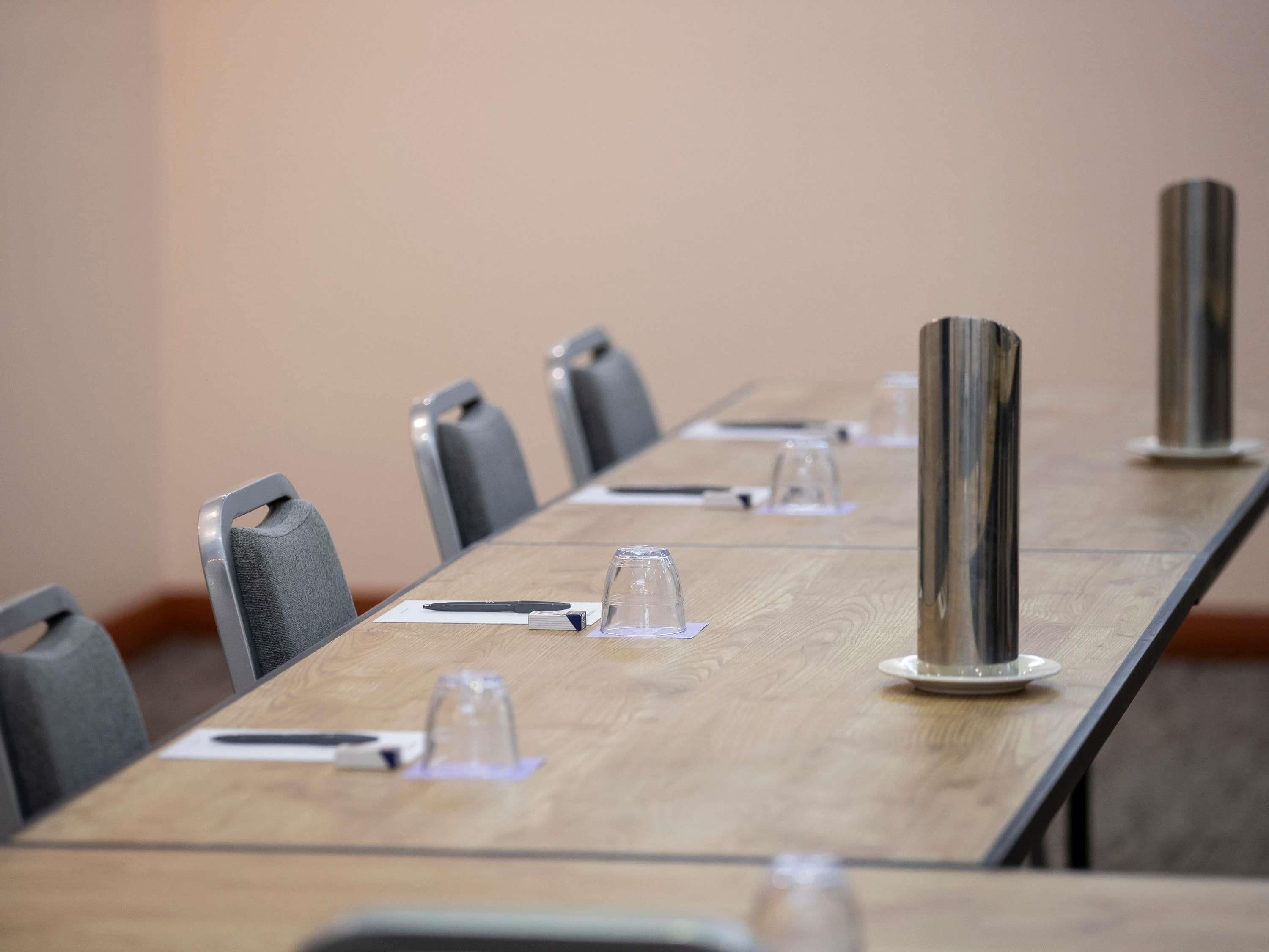 Une salle de conférence avec une longue table, des chaises et quelques objets en verre.