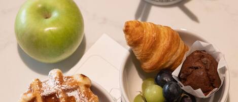 Un plato con una manzana verde, un gofre, un croissant y un muffin con arándanos.