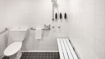 Un baño con inodoro, ducha con cabezal de ducha manual y banco.