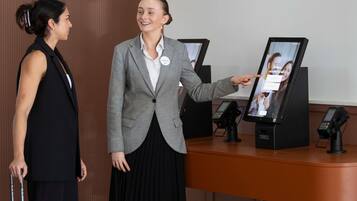 A reception desk with a digital kiosk, a name tag, and a luggage trolley.