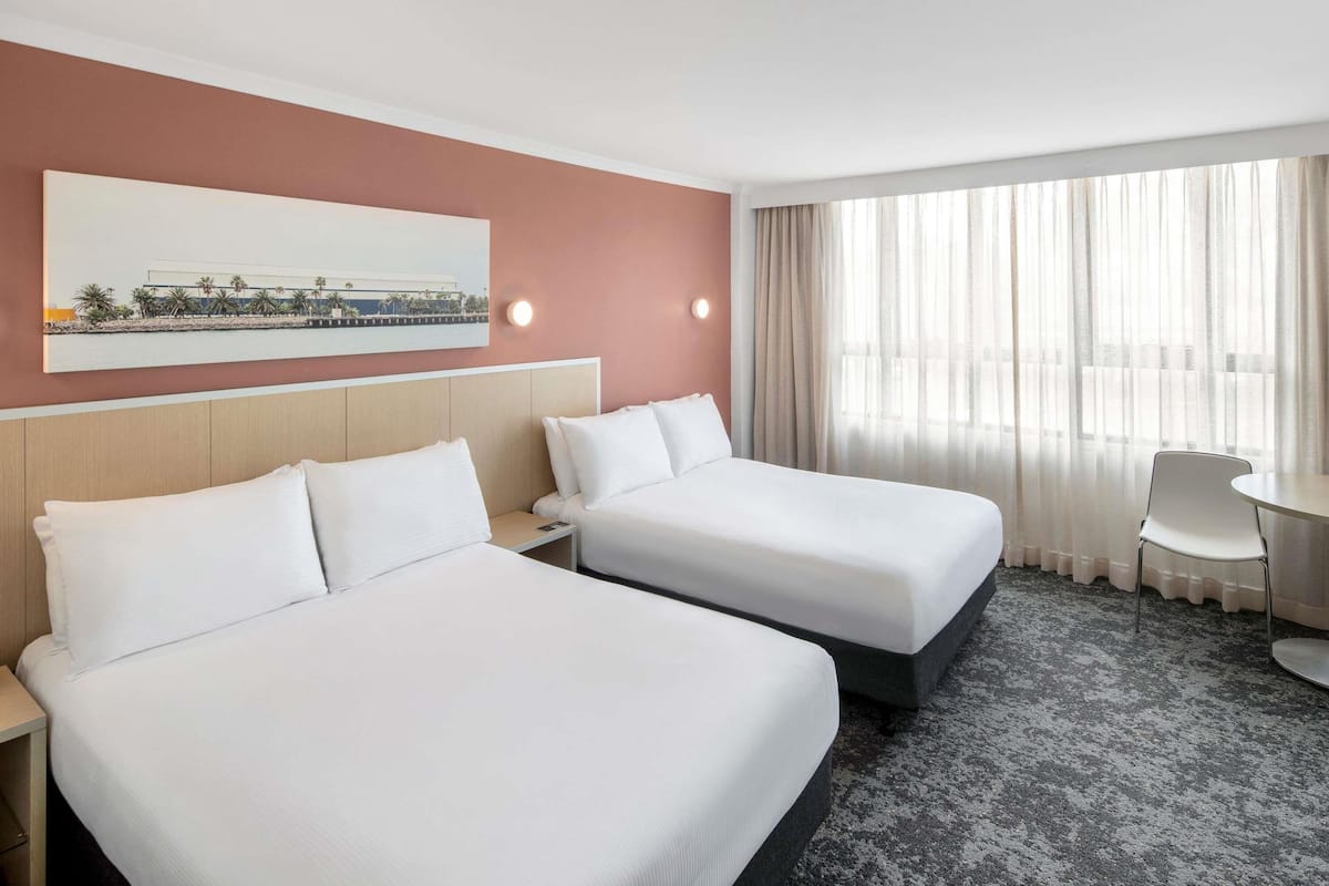 A hotel room with two beds, a desk, a chair, and a large window with curtains.
