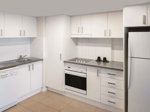 A modern kitchen with white cabinets, a stainless steel refrigerator, a built-in oven, and a sink with a faucet. - Mercure Newcastle (Newcastle West)