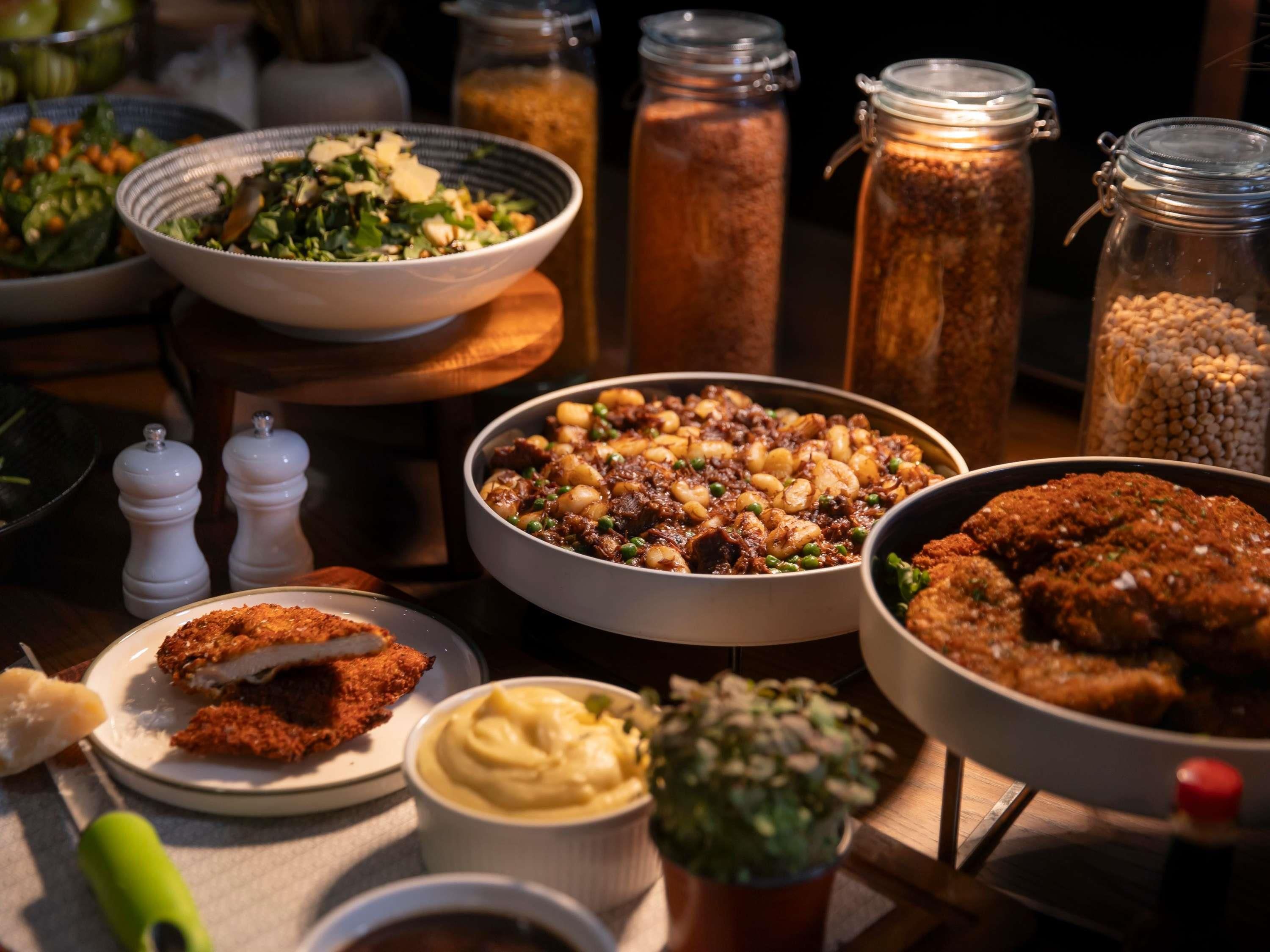 A table with various dishes, including a bowl of stew, a plate of fried chicken, and jars of spices.