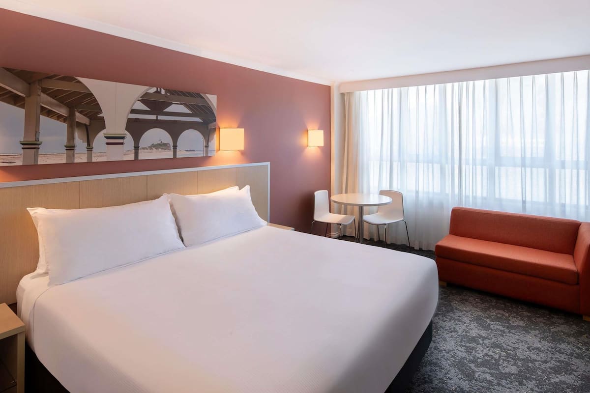 A hotel room with a large bed, a small table with two chairs, a sofa, and a painting on the wall.