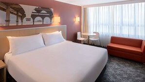 A hotel room with a large bed, a small table with two chairs, a sofa, and a painting on the wall. - Mercure Newcastle (Newcastle West)