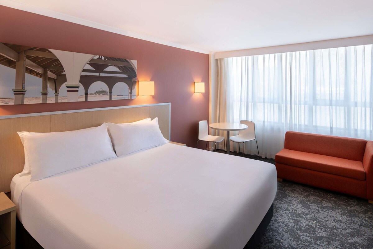 A hotel room with a large bed, a small table with two chairs, a sofa, and a painting on the wall.