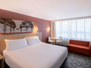 A hotel room with a large bed, a small table with two chairs, a sofa, and a painting on the wall.