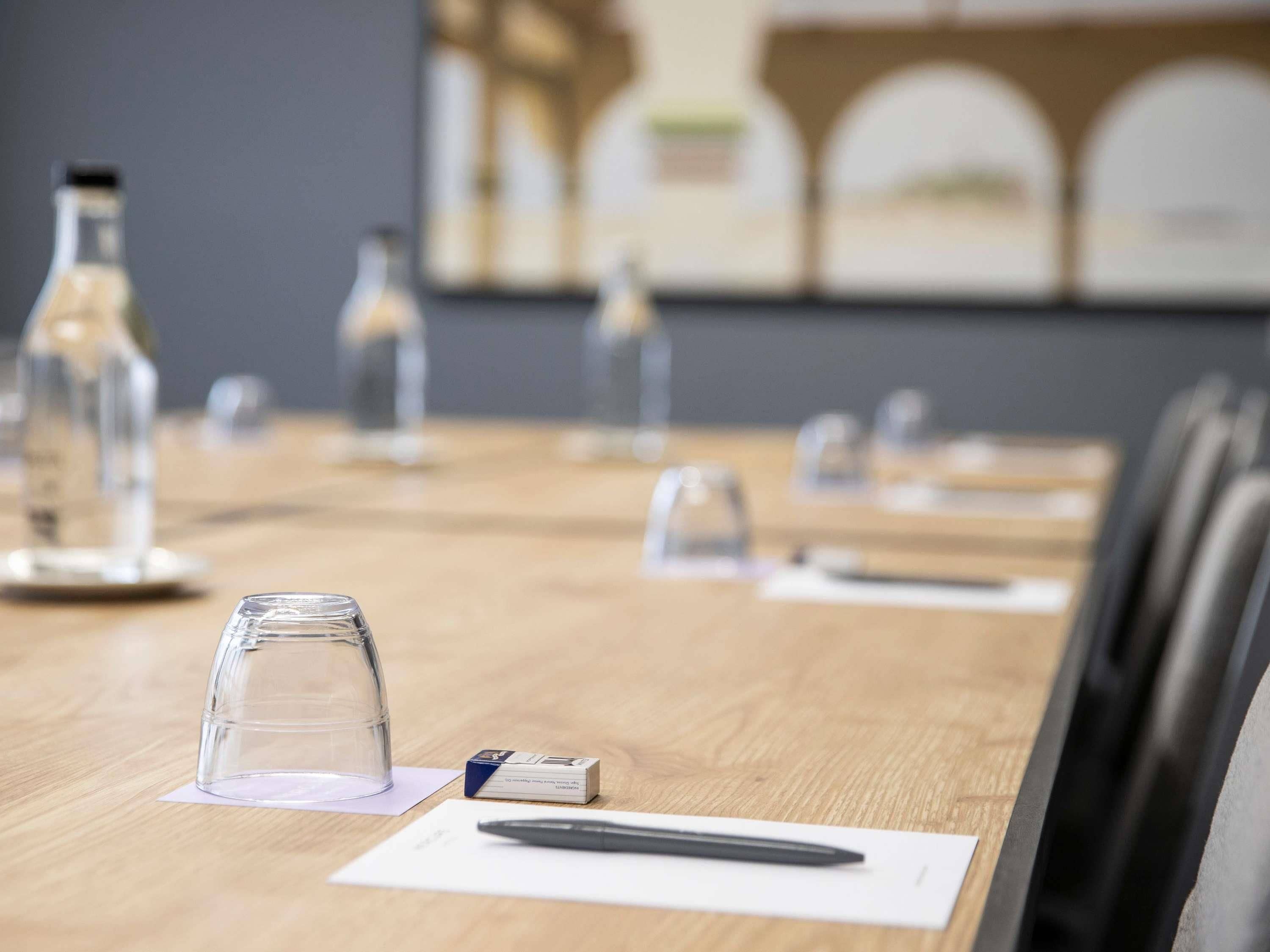 A conference room with a wooden table, clear glass water bottles, a pen, and a box of tissues.