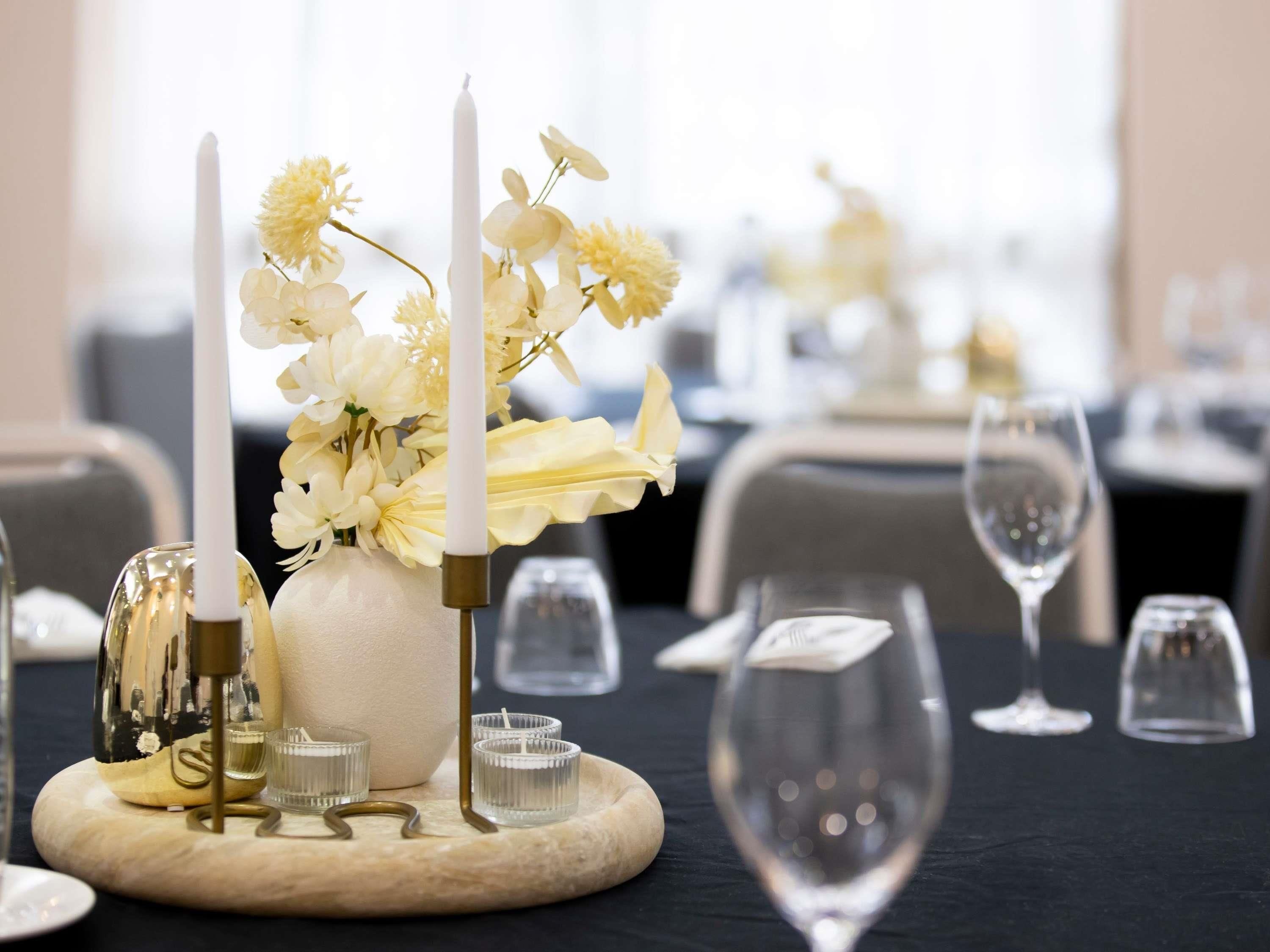 A table setting with a vase of flowers, candles, and glasses.