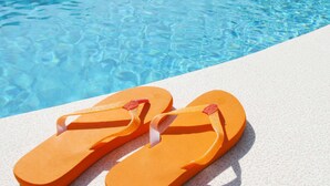 Un paio di ciabatte arancioni su una superficie bianca e ruvida, vicino a una piscina cristallina.