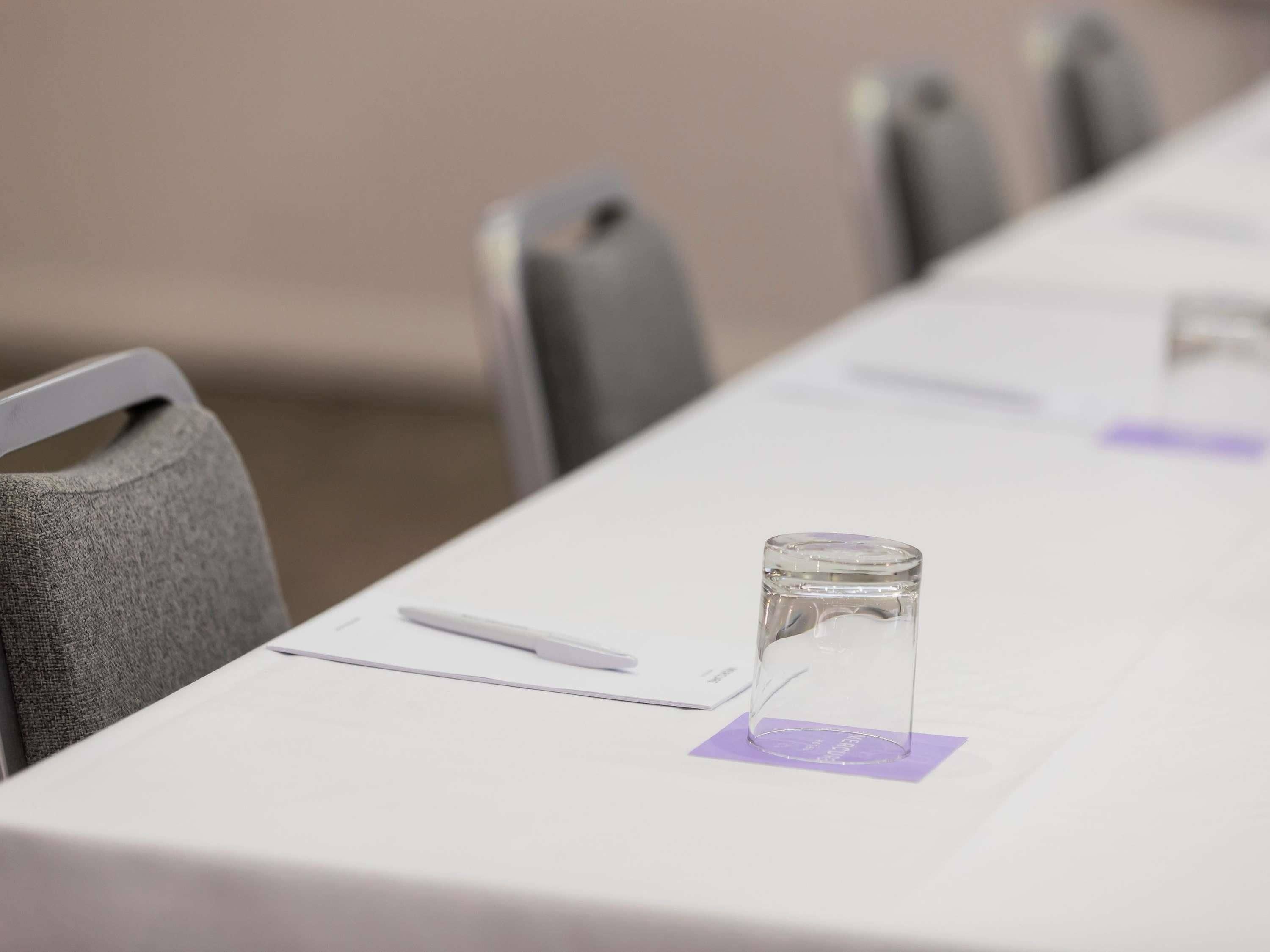 A conference table with a glass, a pen, and a notepad.