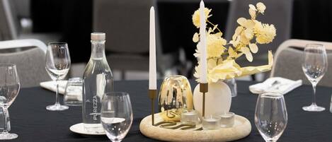 A dining table set with wine glasses, a bottle, a candle, and a centerpiece with flowers and a decorative item.