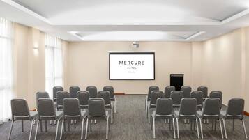 Ein Konferenzraum mit grauen Stühlen, einer Projektionsleinwand, auf der 'MERCURE HOTEL NEWCASTLE' zu sehen ist, und einem Teppichboden.
