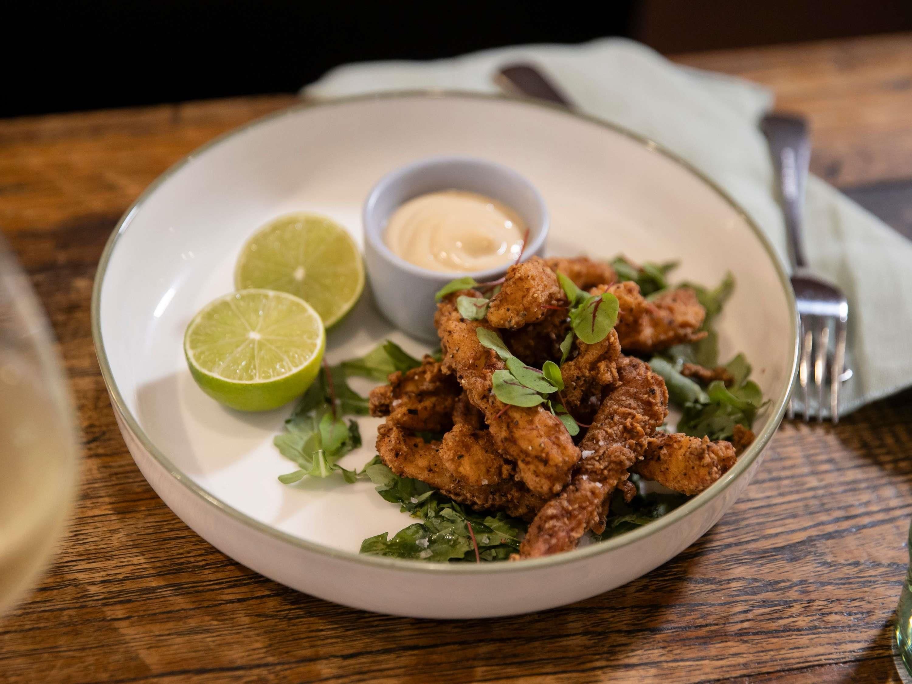 A plate of fried chicken with a side of dipping sauce and lime.