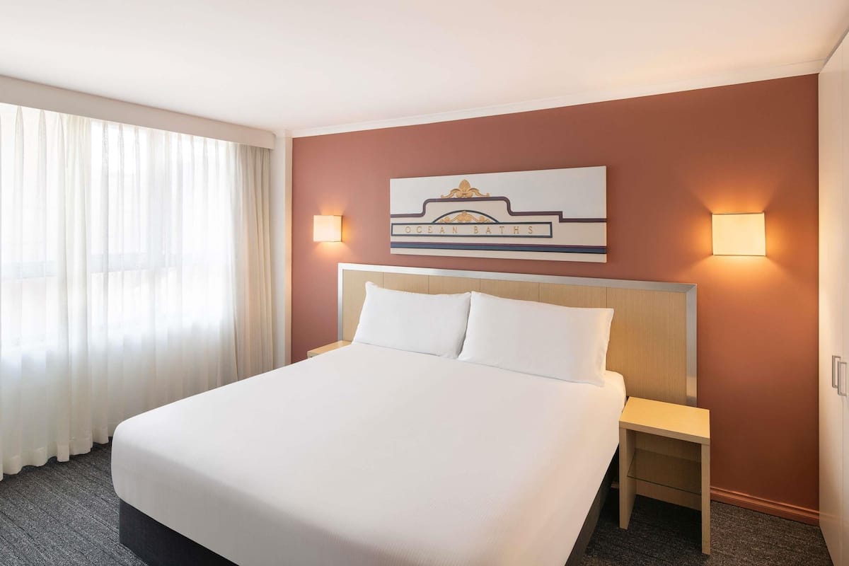 A hotel room with a large bed, two bedside tables, a wall-mounted sign, and a window with curtains.